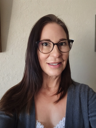 Before photo of a smiling woman wearing glasses and a grey cardigan, captured indoors with natural light.