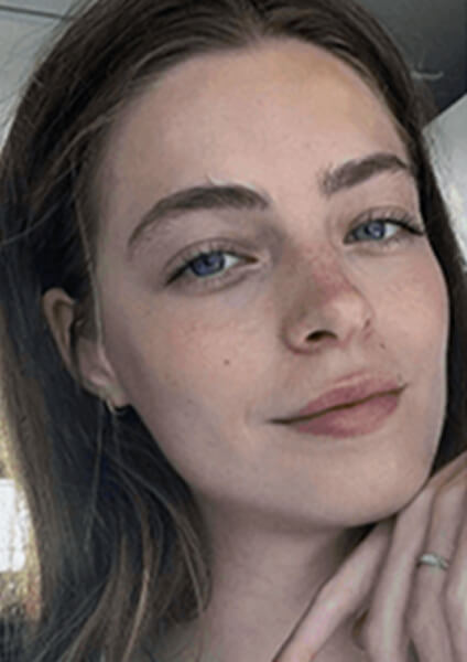 Natural-light selfie of a young woman with blue eyes, long brown hair, and a soft smile, taken before AI headshot generation.