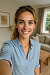 Smiling woman in blue tshirt taking selfie in a cozy indoor setting.