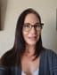 Before photo of a smiling woman wearing glasses and a grey cardigan, captured indoors with natural light.