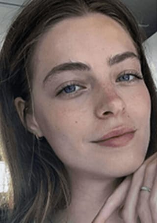 Natural-light selfie of a young woman with blue eyes, long brown hair, and a soft smile, taken before AI headshot generation.