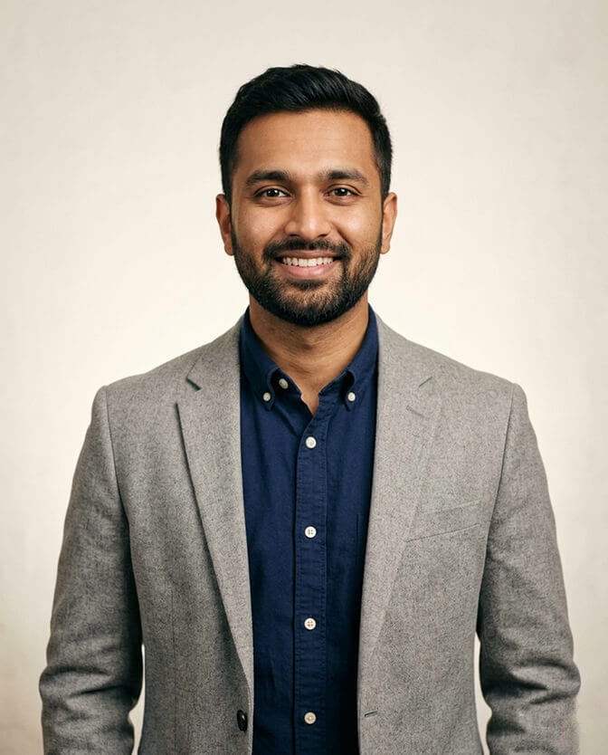Professional AI headshot of a man in a gray blazer and navy shirt against a soft neutral background with a relaxed genuine smile showing how the right tool produces the authentic version of you the camera kept hiding