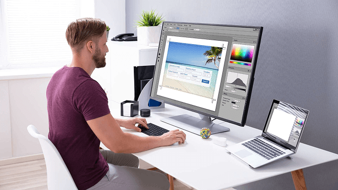 Man at a desk editing a photo in desktop software, adjusting crop and colour before uploading it as a LinkedIn profile picture