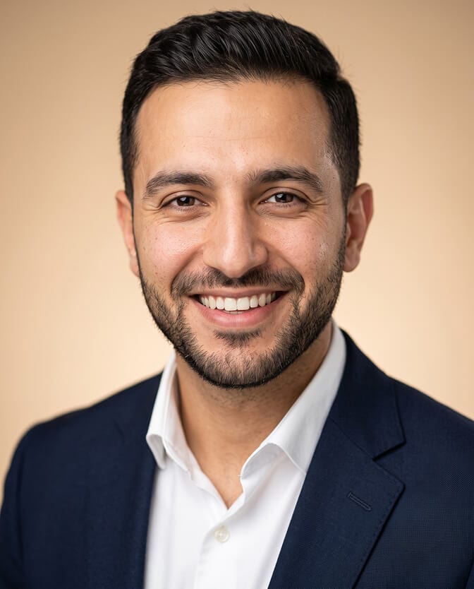 Approachable smiling male CEO headshot: executive with a full, natural smile in a navy blazer and open white shirt against a warm beige background