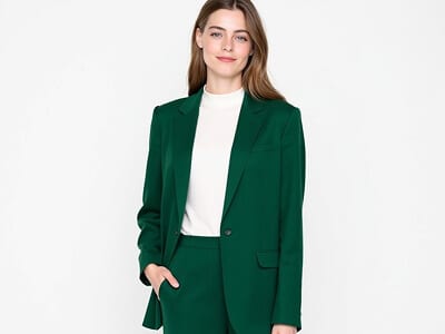Deep green blazer passport photo outfit example for a woman, worn over a white top against a plain background