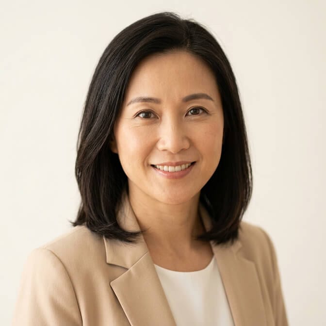 Professional iPhone style headshot of a woman in a beige blazer and white top against a clean cream background showing the natural facial proportions that emerge when the camera is shot from a respectful distance