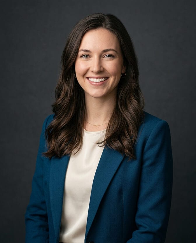 Professional AI headshot of a woman in a deep teal blazer and cream top against a dark studio background showing the calm, present expression of someone who is not camera shy