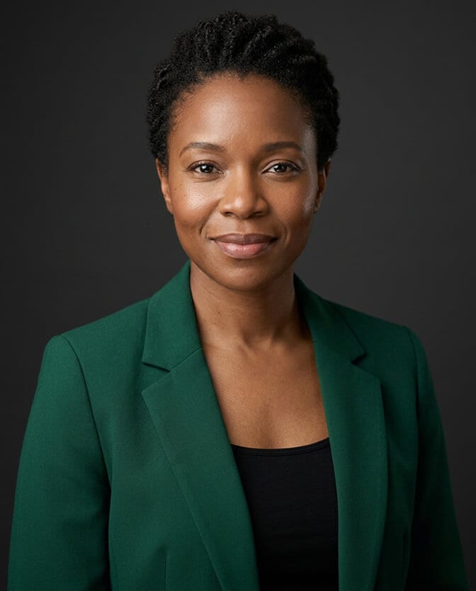 Professional headshot of a woman in a solid emerald green top against a clean neutral background showing how a simple fitted solid color frames the face and removes distraction