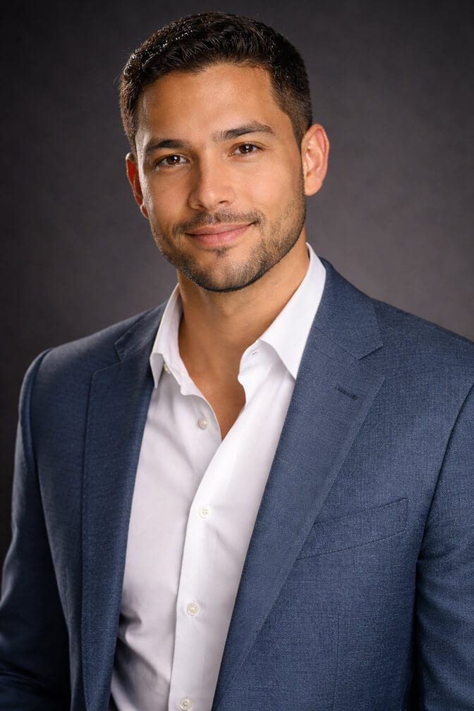 Professional AI headshot of a man in a blue blazer and white open collar shirt against a dark studio background showing the polished confident look that emerges once the seven conditions are fixed