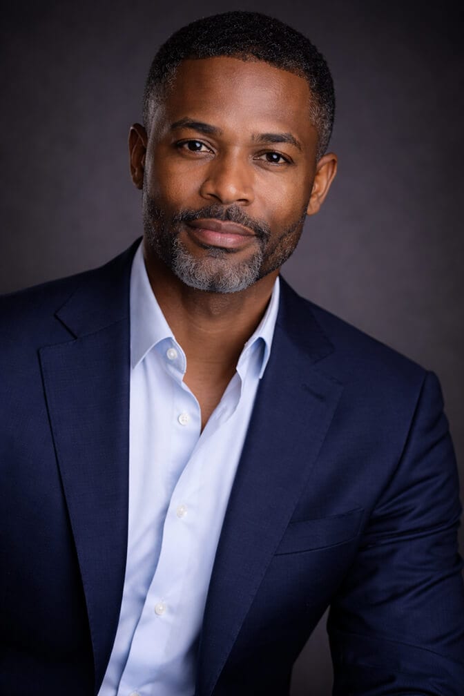 Realistic professional headshot of a man in a navy suit that reads simply as a good headshot
